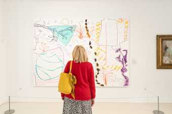 A person looks at an artwork by Rose Wylie with their back to the camera