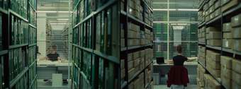 Two images of a person at a desk in a room full of shelves stacked high with folders and boxes