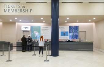 A person waiting by a large grey desk with 'Tickets and Membership' written above it