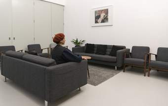 A person sitting on a grey sofa in a room with sofas, chairs, a rug, a plant and a picture on the wall