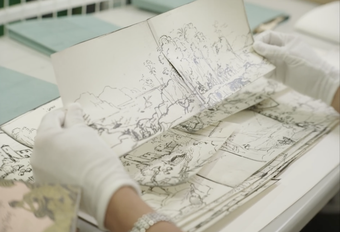 Hands in white gloves holding a landscape drawing on paper